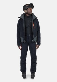 Completo da sci con giacca blu navy con dettagli grigi, tasche con zip, strato base nero e pantaloni abbinati. Include un casco nero e occhiali da sci.