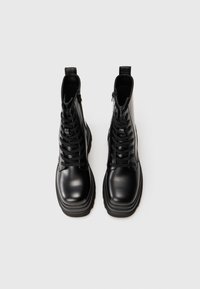 Botines negros de tobillo hechos de cuero suave, con punta redonda, cordones en la parte delantera, cremallera lateral y suela de goma gruesa.