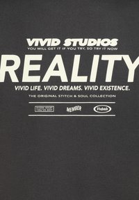Black cotton T-shirt featuring bold white text: "VIVID STUDIOS," "REALITY," and additional phrases. Simple design with a smooth texture.