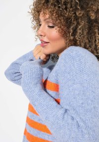 Maglione lavorato a maglia di colore azzurro chiaro con strisce arancioni e grigie. Presenta una vestibilità morbida e polsini a coste, evidenziando un tessuto morbido e texturizzato.