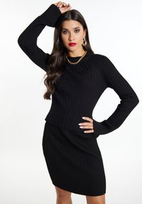 Schwarzes, geripptes Strickkleid mit langen Ärmeln und weitem Ausschnitt. Besitzt einen strukturierten Stoff und eine figurbetonte Passform, die die Silhouette betont. Trägt eine goldene Kettenhalskette.