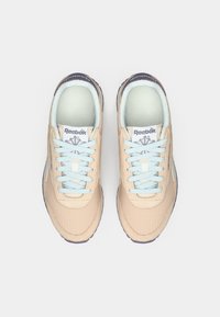 Bežīgas Reebok kedas ar gaiši zilu auklu, baltu iekšējo odere un tumšiem zoliem, skatītas no augšas uz baltas fona.