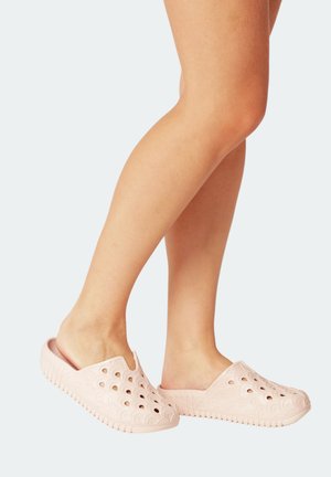 Zoccoli rosa chiaro slip-on realizzati in gomma con una superficie testurizzata, caratterizzati da ritagli circolari e un design decorato lungo i lati.