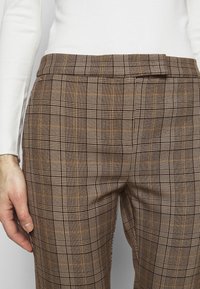 Pantalon à carreaux marron combinant de grands et petits carreaux avec des accents orange. Taille ajustée avec une texture lisse et une coupe sur mesure.