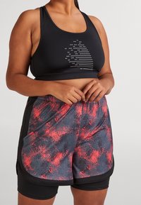 Svart sport-bh med prickad logotyp och shorts i röd och svart mönster med en trimdesign och resårmidja.