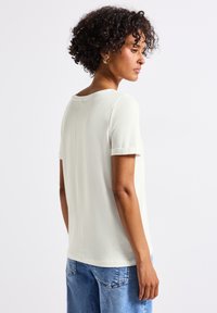 Haut à manches courtes crème clair avec un col rond et un design de dos sans couture. porté avec un jean en denim bleu ample. Texture douce, silhouette décontractée.