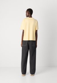 T-shirt jaune à manches courtes avec une coupe décontractée, associé à un jean en denim noir ample, doté d'un design classique à cinq poches.