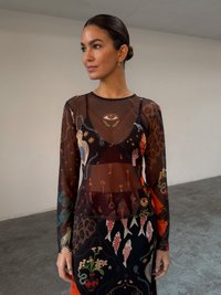 Διαφανής μπλούζα με μακρύ μανίκι και ζωντανά μικτά σχέδια, με μοτίβα ματιών, λουλουδιών και ζώων. Συνδυάζεται με μια πολύχρωμη φούστα με σχέδια.