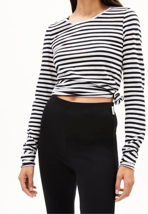 Femme portant un haut à manches longues rayé horizontalement noir et blanc noué à la taille, associé à un pantalon noir taille haute.