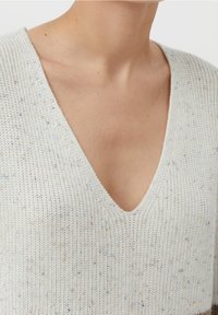 Jasnoszary sweter z dzianiny z dekoltem w kształcie litery V, ozdobiony wielokolorowymi plamkami na całej powierzchni. Miękka faktura i luźny krój, widoczne krótkie rękawy.