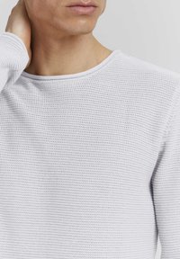 Hellgrauer, strukturiert gestrickter Pullover mit Rundhalsausschnitt, der ein dezentes Muster und gerippte Bündchen aufweist, vor einem neutralen Hintergrund platziert.