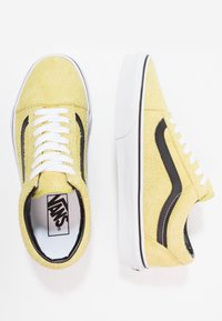Baskets Vans en daim jaune avec lacets blancs, bande latérale noire et semelles en caoutchouc blanches, vues de dessus et de côté.