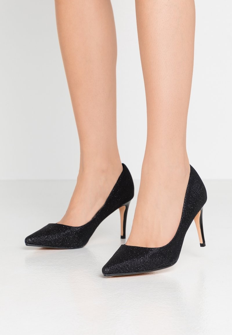 Chaussures à talons hauts noires avec un bout pointu et une tige en tissu texturé. Elles possèdent un talon stiletto fin et une semelle lisse.