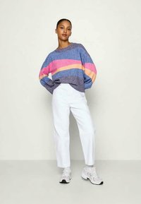 Sinine kudum, millel on roosa ja kollane triip, koos valgete sirgete pükste ja hallide tossudega.