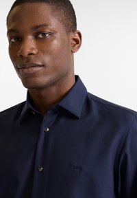Marineblauwe button-up shirt met een gestructureerde kraag, textuurstof en subtiele logo borduring. Beschikt over twee knoopsluitingen bij de kraag.