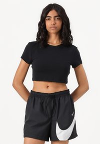 Melna īsa krekla ar īsām piedurknēm kombinācija ar melnām šortiem, kuriem ir balts Nike logo un izliekts balts akcentu sānos.