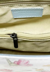 Interno beige di una borsa con una tasca con zip e un tirante nero. L'etichetta recita "Vera Pelle Prodotta in Italia". Texture liscia.