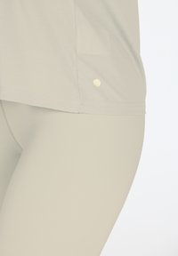 Maglietta grigia chiara a maniche corte con uno spacco laterale e un piccolo accento giallo all'orlo, abbinata a leggings grigi chiari. Texture liscia.