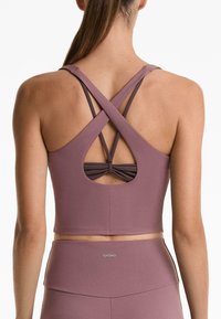 Mauve sportski crop top s ukriženim trakama i izrezom na leđima. Glatka tekstura s tijesnim fitom. Prikazana marka na rubu.