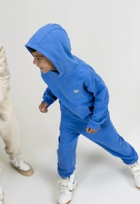 Blauwe hoodie met bijpassende broek van zachte stof, met een klein logo. De outfit heeft elastische boorden en een zak aan de voorkant.
