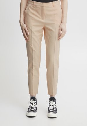 Pantaloni beige chiaro con gamba affusolata e finitura liscia, con passanti per cintura e tasche laterali, abbinati a sneakers nere alto-topp.