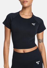 Czarny skrócony top sportowy z krótkimi rękawami i okrągłym dekoltem. Posiada biały logo na klatce piersiowej oraz gładką, elastyczną strukturę tkaniny.