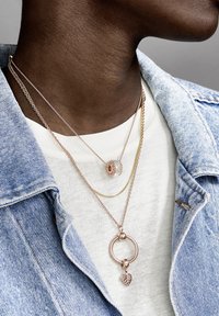 Collane a tre strati con tonalità di oro rosa e argento. Una con un pendente circolare, un'altra con un anello testurizzato e una sottile catena d'oro.