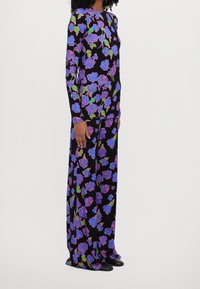 Kwiatowa sukienka z długim rękawem na czarnym tle, z dużymi niebieskimi i różowymi różami, zielonymi liśćmi oraz luźnym krojem. Gładka faktura materiału.