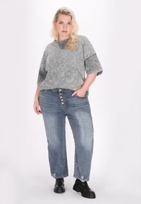 Grå oversized kortærmet skjorte med en falmet struktur, parret med slidte blå jeans med knaplukning og ankelhøje sorte støvler.