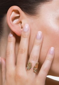 Gouden ring met een gestructureerd ontwerp en gefloteerde details. Draagt op de vingers, wat de elegante vakmanschap en de gladde afwerking benadrukt.