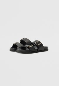 Sandale negre, tip slip-on, fabricate dintr-un material neted, având două curele late cu catarame metalice pătrate și o talpă plată din cauciuc.