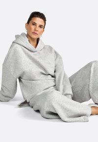 Felpa grigia con cappuccio e pantaloni della tuta abbinati, realizzati in tessuto morbido, caratterizzati da una vestibilità comoda, cappuccio e polsini a costine, con dettagli testurizzati sottili.