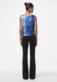 Top court en sequins bleus avec un décolleté en scoop et sans manches, associé à un pantalon noir évasé, vu de dos.