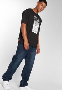 Zwarte katoenen t-shirt met grafische print, gecombineerd met donkerblauwe spijkerbroeken. Accessoires zijn witte sneakers en een kleurcontrast label.