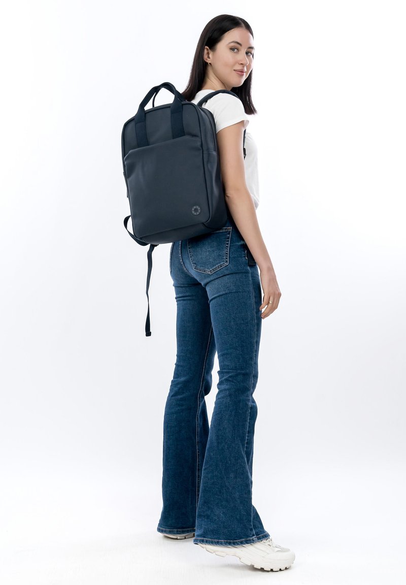 Marineblauwe rugzak met een gladde textuur, voorzien van dubbele bovenhandvatten en verstelbare schouderbanden, getoond op een persoon.