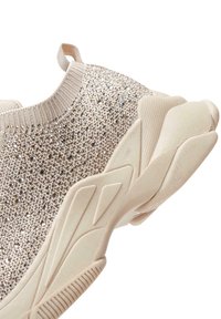 Zapatilla deportiva beige con un upper de tejido brillante, acentos texturizados y una suela blanca gruesa con patrones estriados.