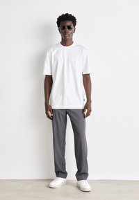 Tricou alb cu mânecă scurtă, având un mic logo, asortat cu pantaloni gri tailored și adidași albi. Ochelarii de soare adaugă un detaliu distinctiv.