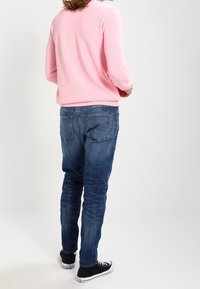 Ljusrosa tröja med strukturerad stickning, kombinerad med blå denimjeans med bakfickor. Svarta sneakers fulländar outfiten.