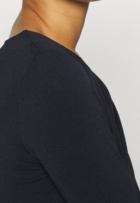 Svart långärmad topp med en figurnära design. Slät textur, minimal sömmar och en rundad halsringning som betonar en smickrande silhuett.