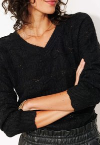 Pull en tricot noir avec un col en V, motif texturé et poignets côtelés. Assorti à une jupe noire à taille élastique.