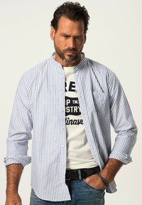 Camicia a maniche lunghe a strisce blu chiaro e bianche con colletto alla cinese, chiusura con bottoni e taschino sul petto, indossata sopra una maglietta con grafica.