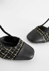 Chaussures slingback en tweed noir texturé avec un design à bout carré et des brides fines à la cheville, sur un fond clair uni.