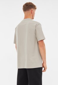 Világosszürke pamut póló rövid ujjakkal, kerek nyakkivágással és laza szabással. Simább, egyszínű textúrájú.