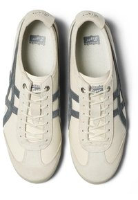 Sneaker in tessuto beige con dettagli in suede grigio, lacci piatti, suola textured e strisce laterali. Logo visibile sulla linguetta.