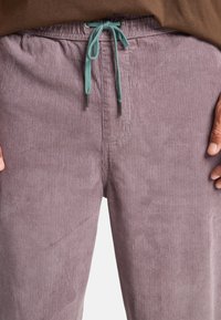 Corduroy pants in muted lavender with a ribbed texture. Features a drawstring waist in teal and metal eyelets. Smooth fabric detail.