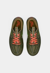 Ζευγάρι ελαιόχρωμων αθλητικών παπουτσιών Nike Air με φωτεινές πορτοκαλί κορδόνες και ανακλαστική ταινία στην γλώσσα, προσανατολισμένα από πάνω σε λευκό φόντο.