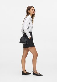 Žena kráča v čiernej koženej minisukni, bielej blúzke s dlhým rukávom, čiernych strapcových balerínkach a s malou čiernou kabelkou cez rameno.