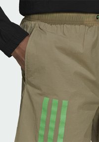 Kaki shorts med elastisk midja, med tre vertikala gröna ränder på sidan. Tyget har en mjuk, lätt textur.