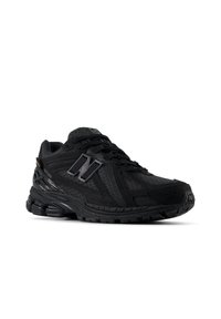 Chaussure de course noire New Balance avec un design texturé, une semelle rembourrée et un grand logo "N" sur le côté, présentée légèrement inclinée sur fond blanc.