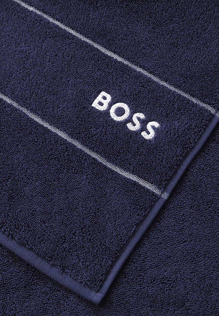 Ciemnoniebieski ręcznik z frotte, białymi paskami i haftowanym logo "BOSS" w rogu. Miękki i chłonny materiał.